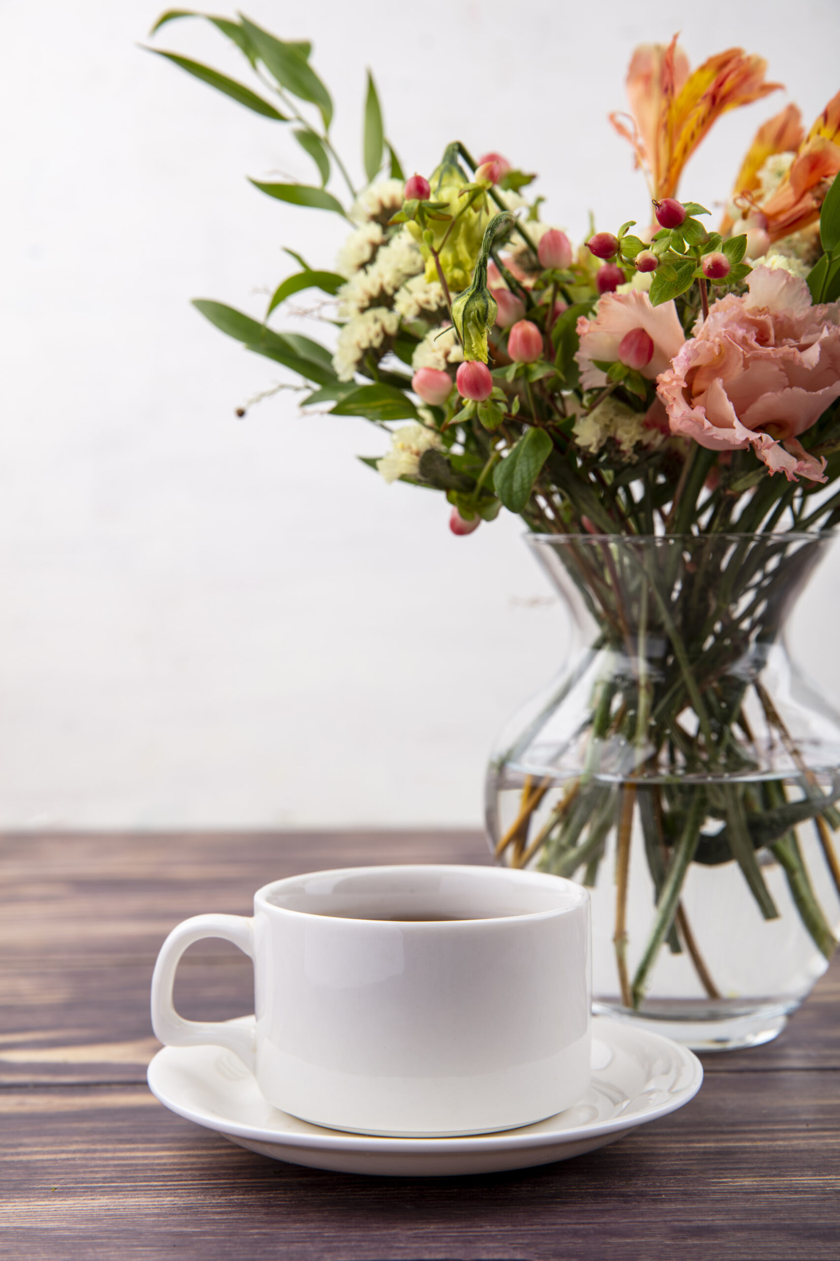 side view of a cup of tea with beautiful flowers on a glass vase on a wooden table on white background
